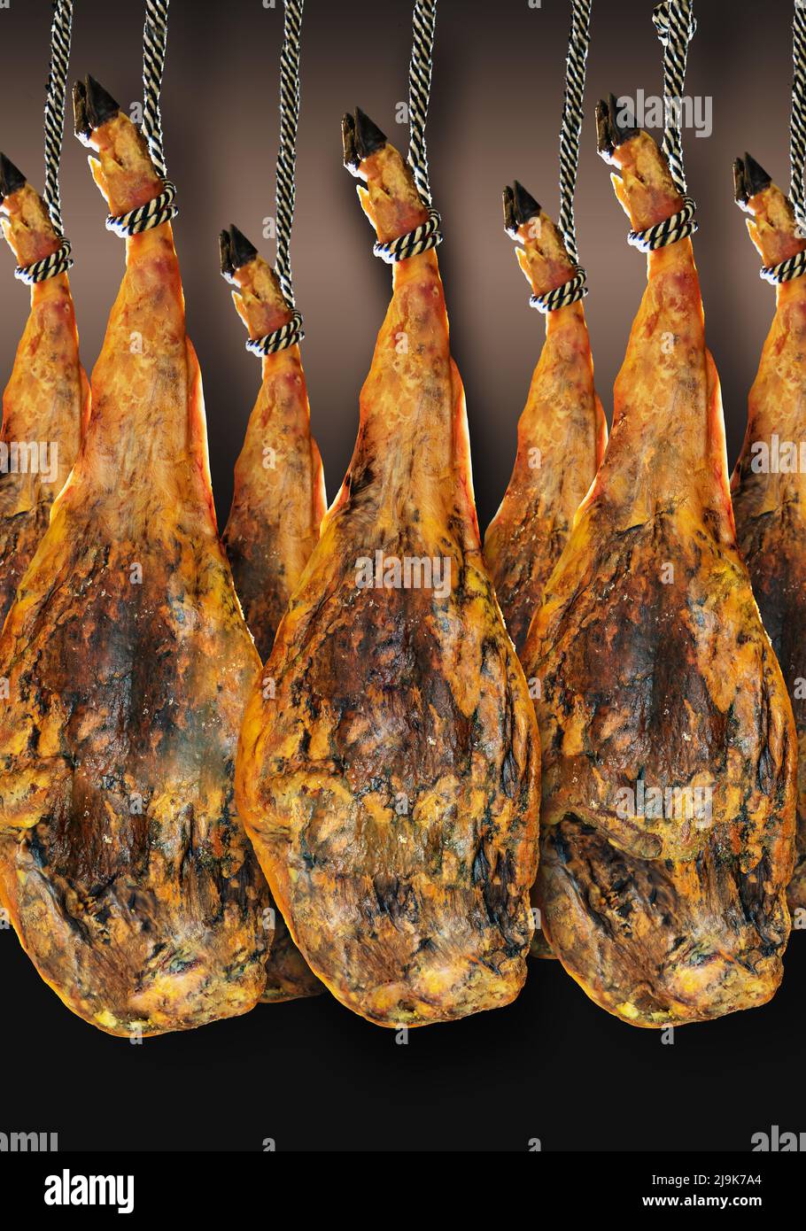Whole leg of several Spanish Iberian serrano ham hanging on a rope, isolated on a stylish gradient background. Stock Photo