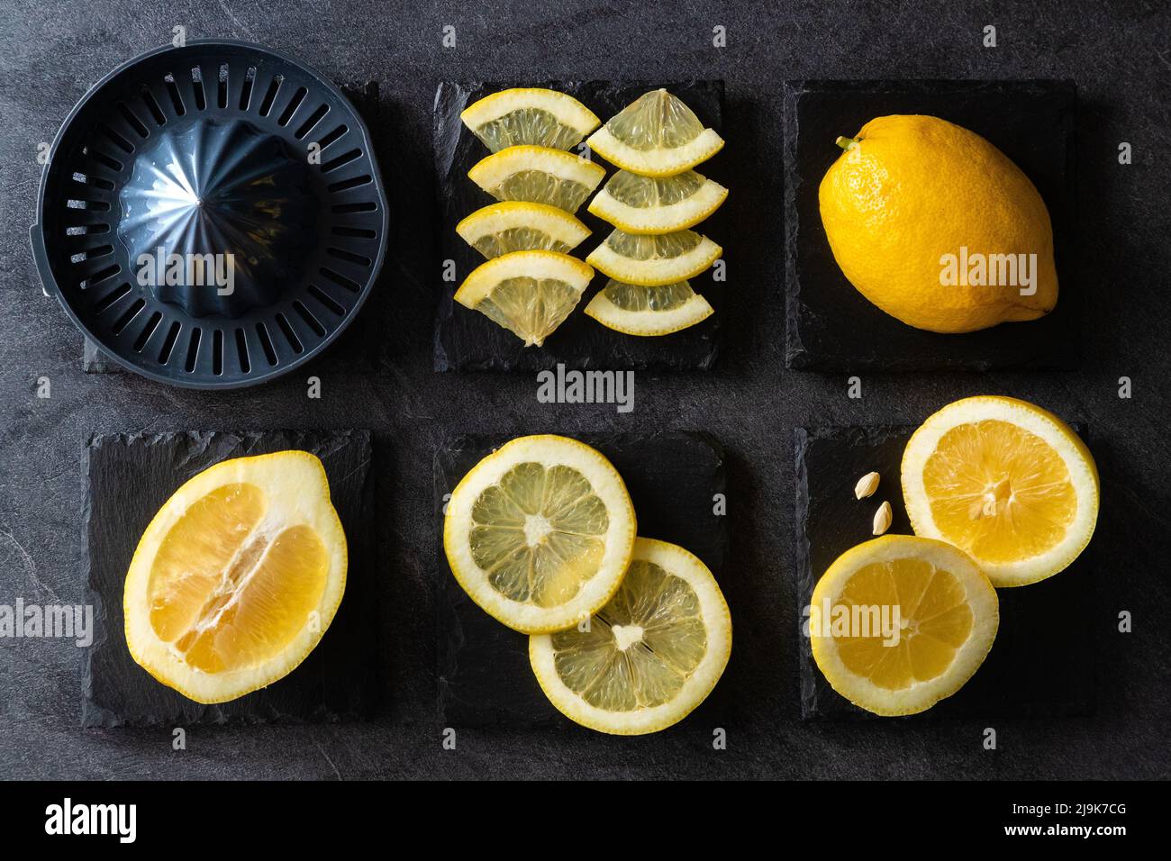 Elegant background design of lemons and lemon slices with squeezer and knife on dark or black cement or stone surface. Stock Photo