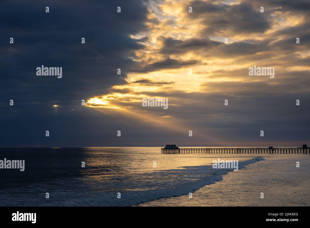 A ray of light shines through the clouds illuminating the Oceanside pier. Stock Photo