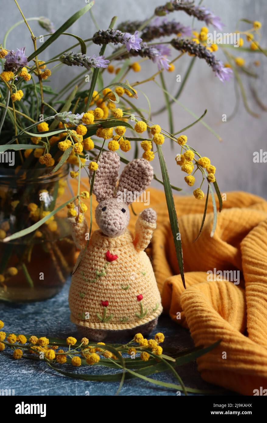 Handmade toys close up. Crochet plant and bunny on grey background. Still life with spring flowers and cute toys. Easter gift ideas. Stock Photo