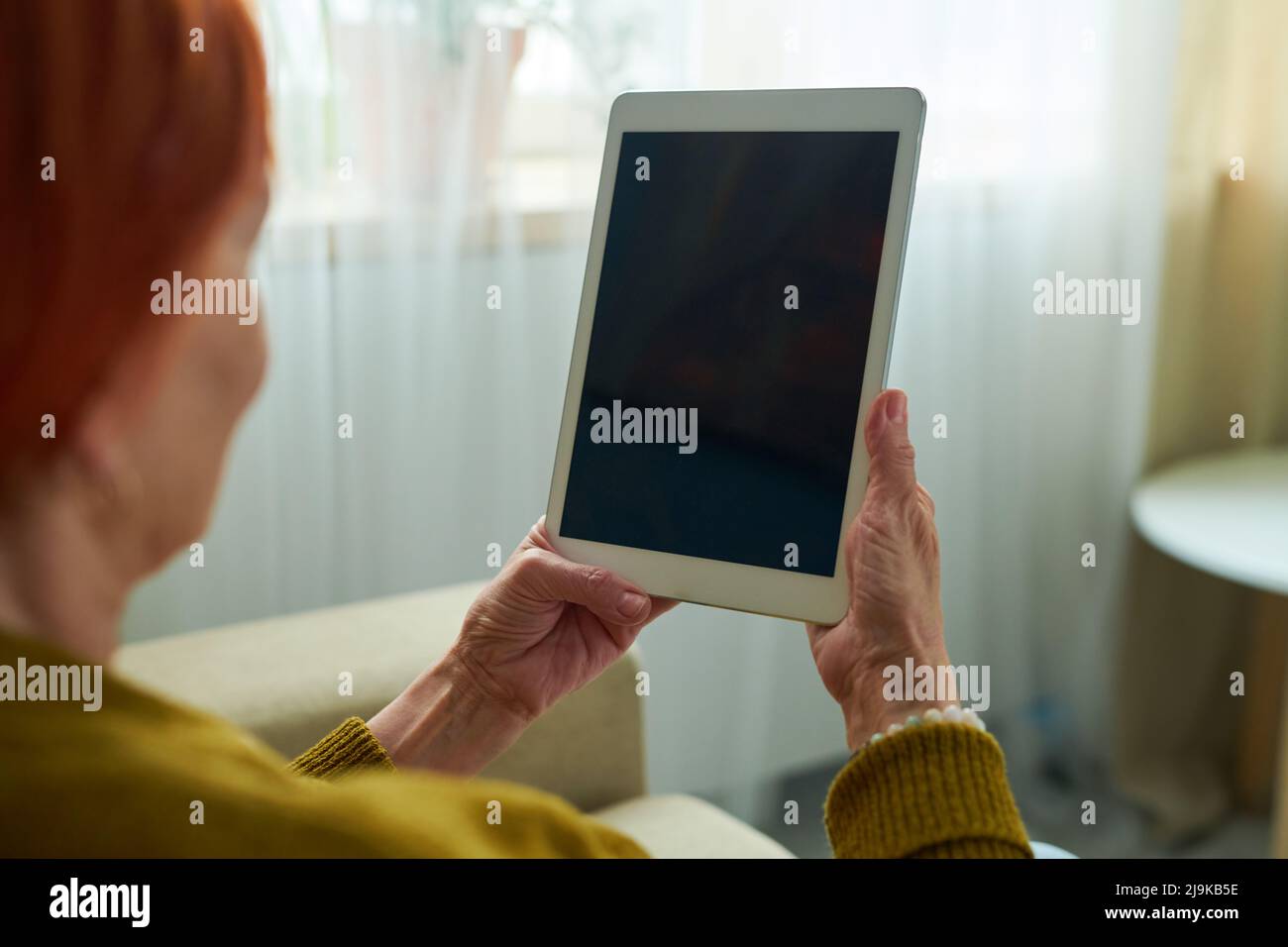 Close-up of elderly woman holding touchpad in front of her face and talking online with her grandchildren Stock Photo