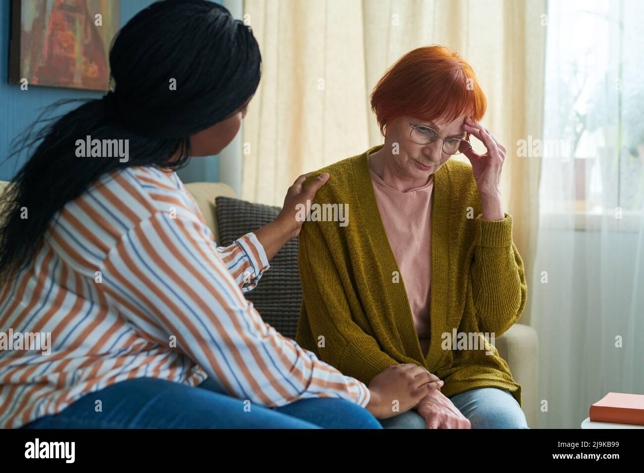 African young caregiver comforting senior woman in depression during her visit at her home Stock Photo
