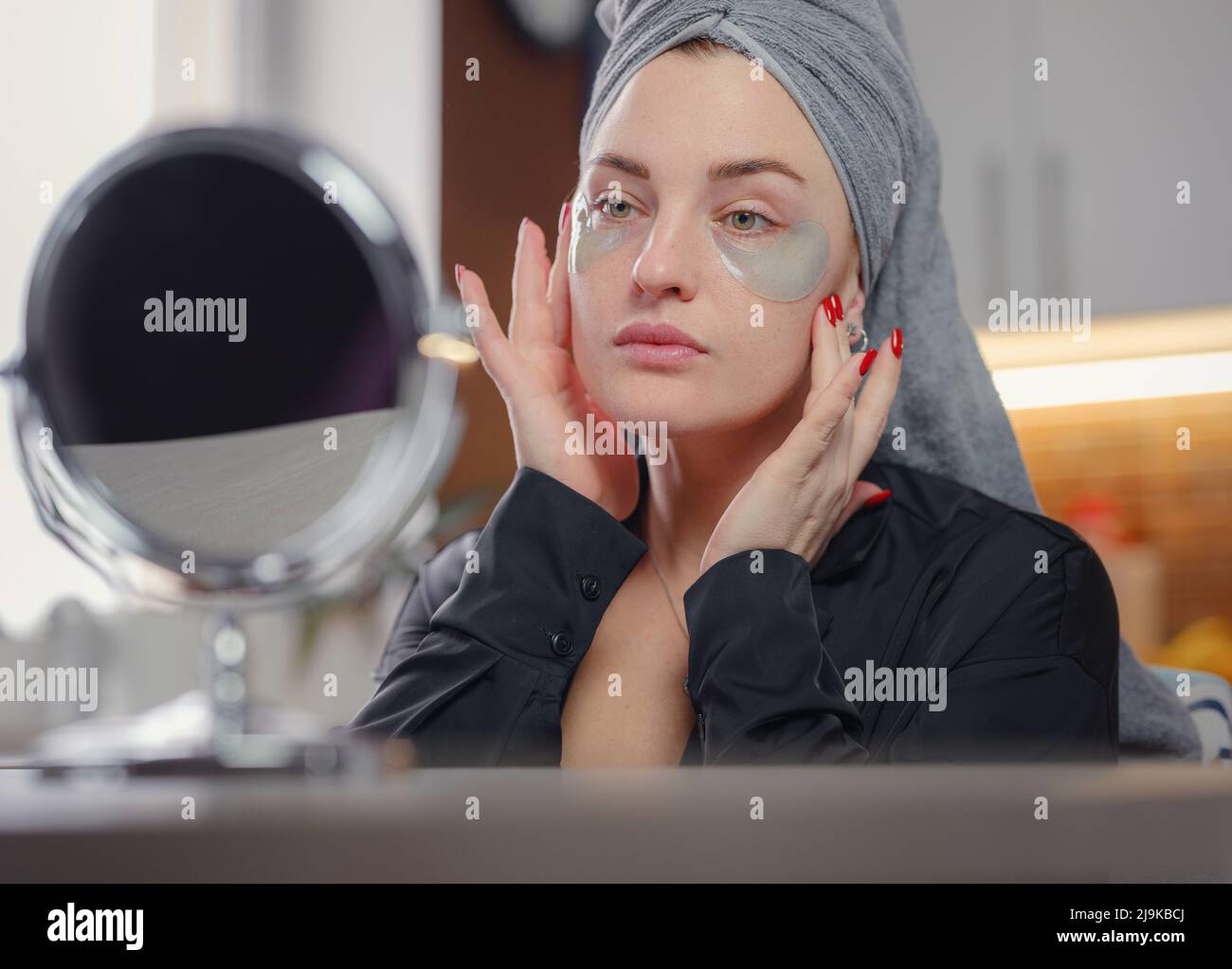 Patches for eyes. Attractive woman in kitchen with towel on her head