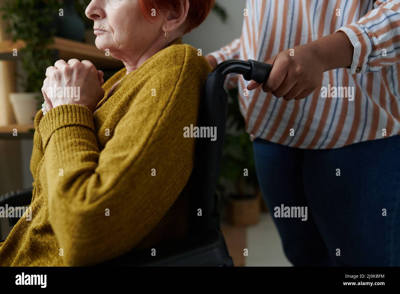 Close-up of senior woman with disability sitting in wheelchair with caregiver standing behind her Stock Photo