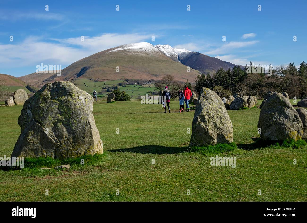 People tourists walkers at Castlerigg Stone Circle, snow topped Blencathra in the background spring late winter Lake District National Park Cumbria UK Stock Photo