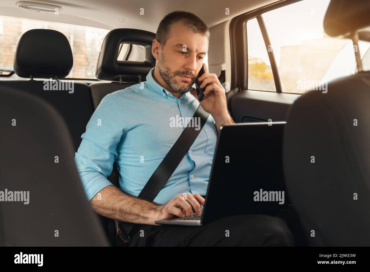 Businessman using laptop talking on smartphone while going by car Stock Photo