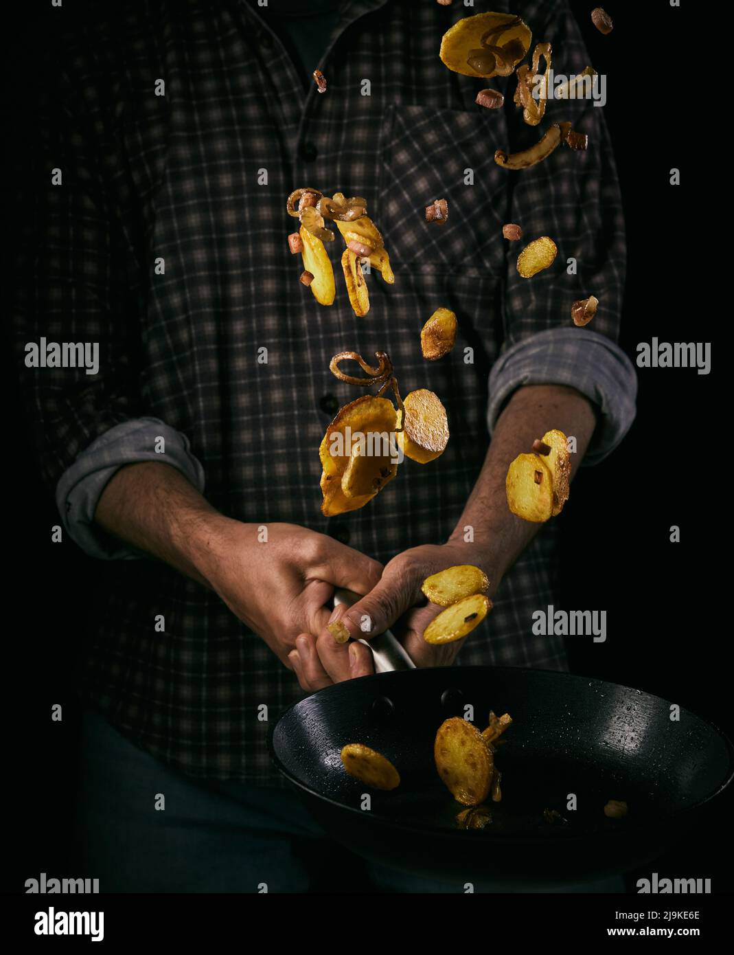 German Bratkartoffeln or fried potatoes throwing trough the air from kitchen chief on black background Stock Photo