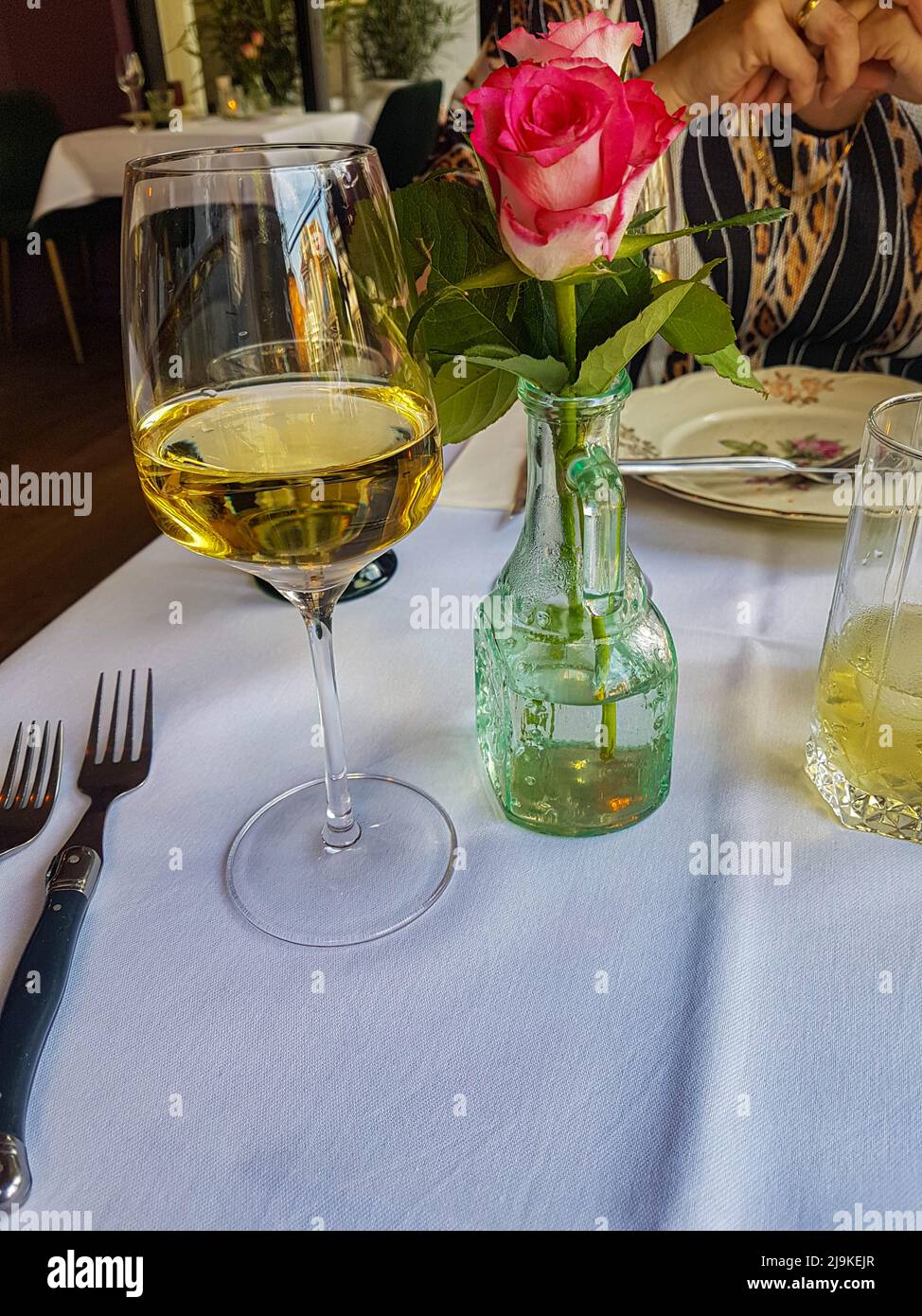 Glass of white wine with a pink rose on a table in a bistro restaurant Stock Photo