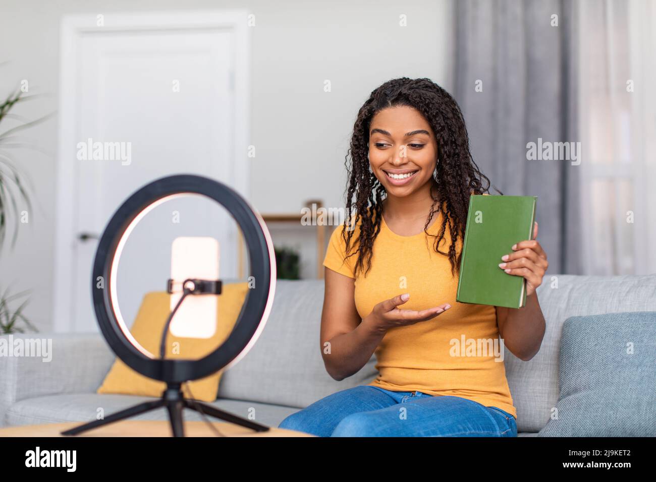Videoblog and technology concept. Positive black female blogger recording video of book review at home Stock Photo