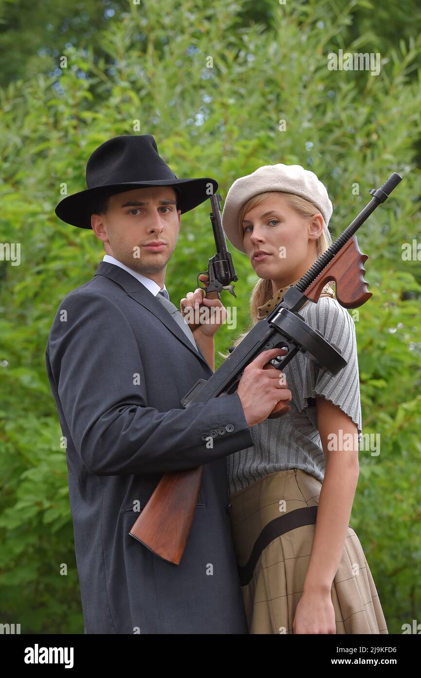 A young couple get dressed up in 1930 style  clothing. They each carry a weapon  as they act the role of the famous gangster  duo Bonnie and Clyde. Stock Photo