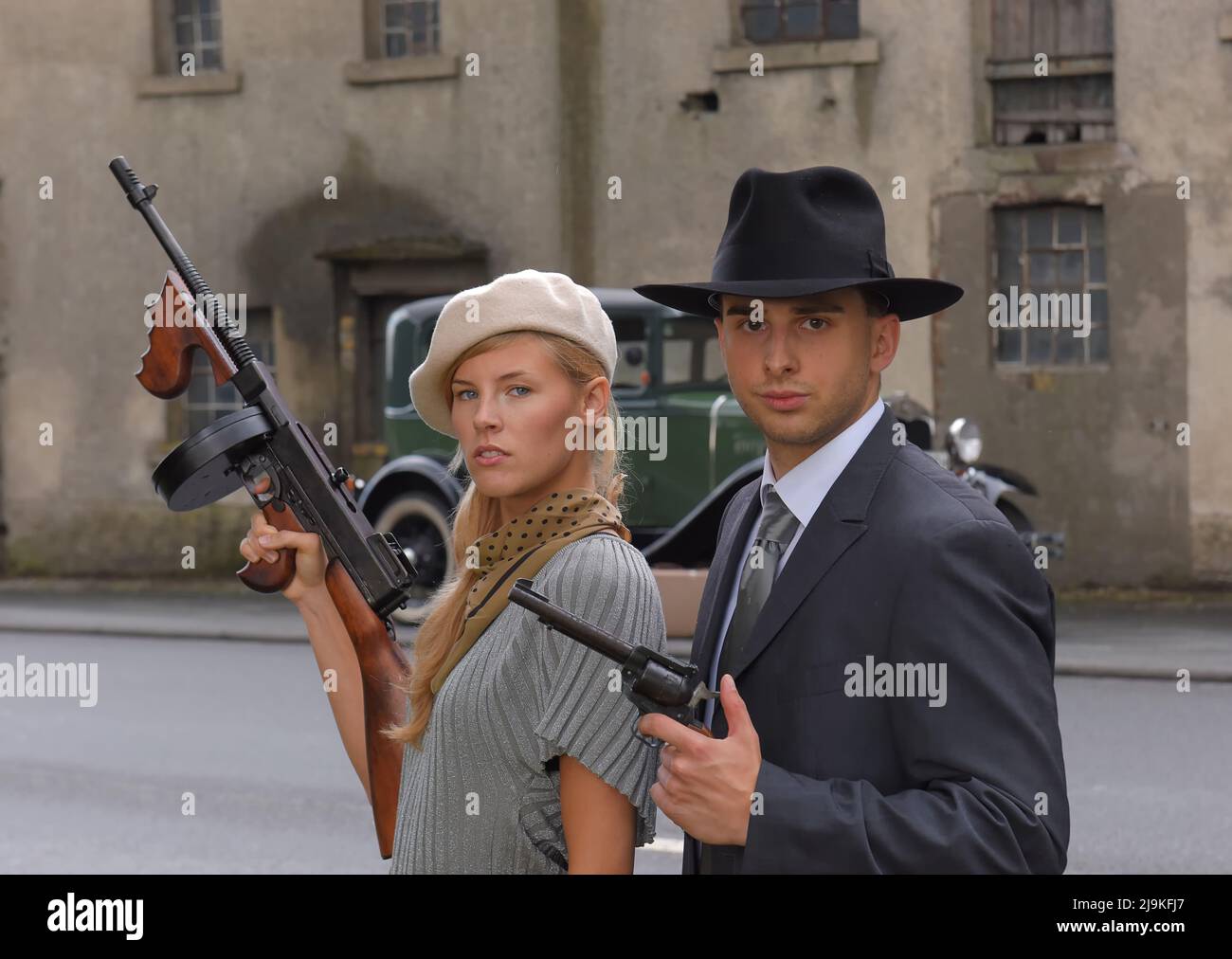 A young couple get dressed up in 1930 style  clothing. They each carry a weapon and act the role of the gangster  duo Bonnie and Clyde. Stock Photo
