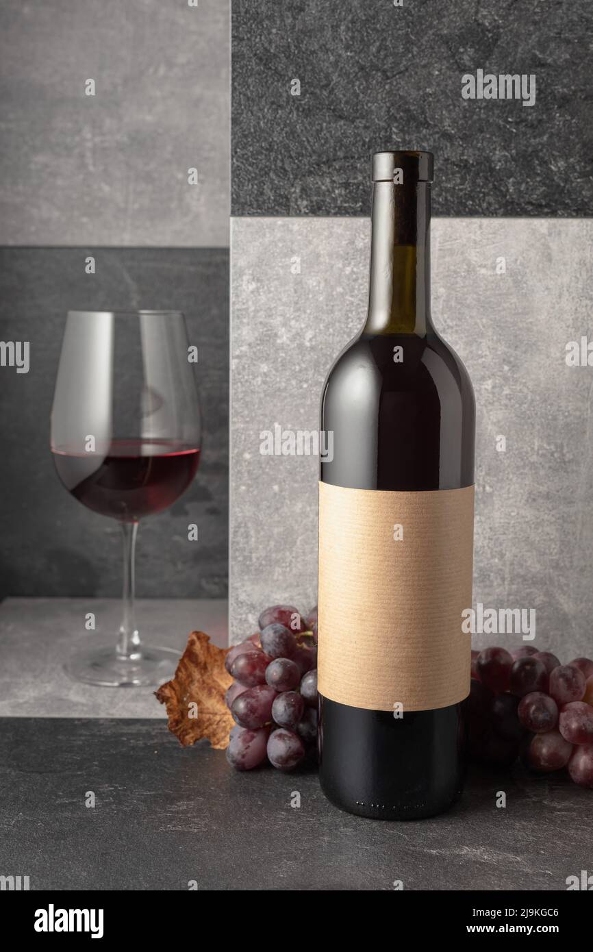Red wine with grapes on a stone background. On a bottle empty label