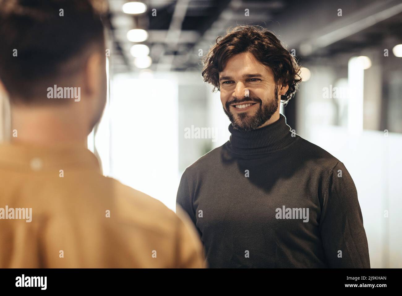 Friendly smiling male colleagues standing face to face, meeting at company hall. Business cooperation concept Stock Photo