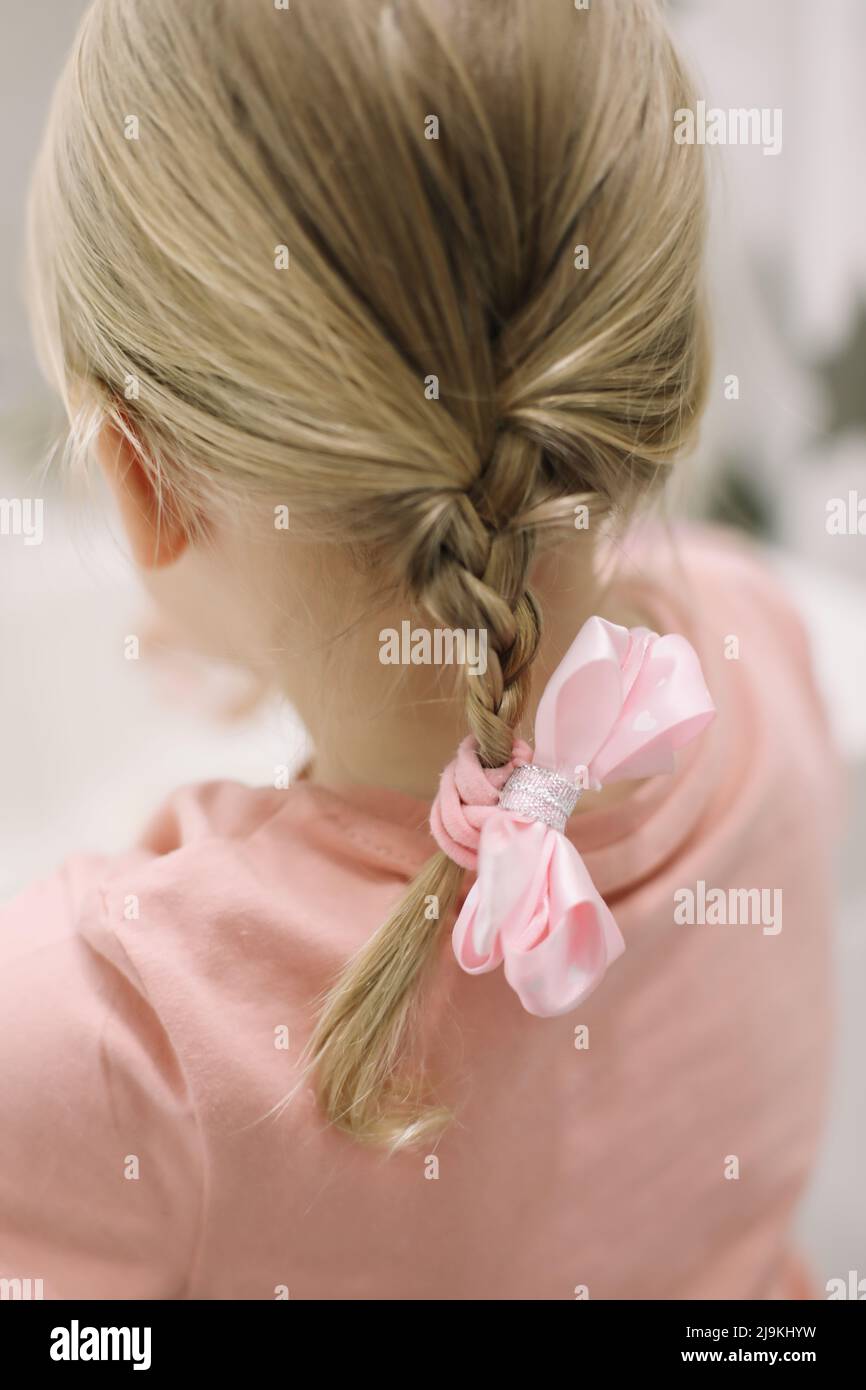 Blonde small girl braid hair with pink ribbon bow. Haircare, hairstyling. Stock Photo