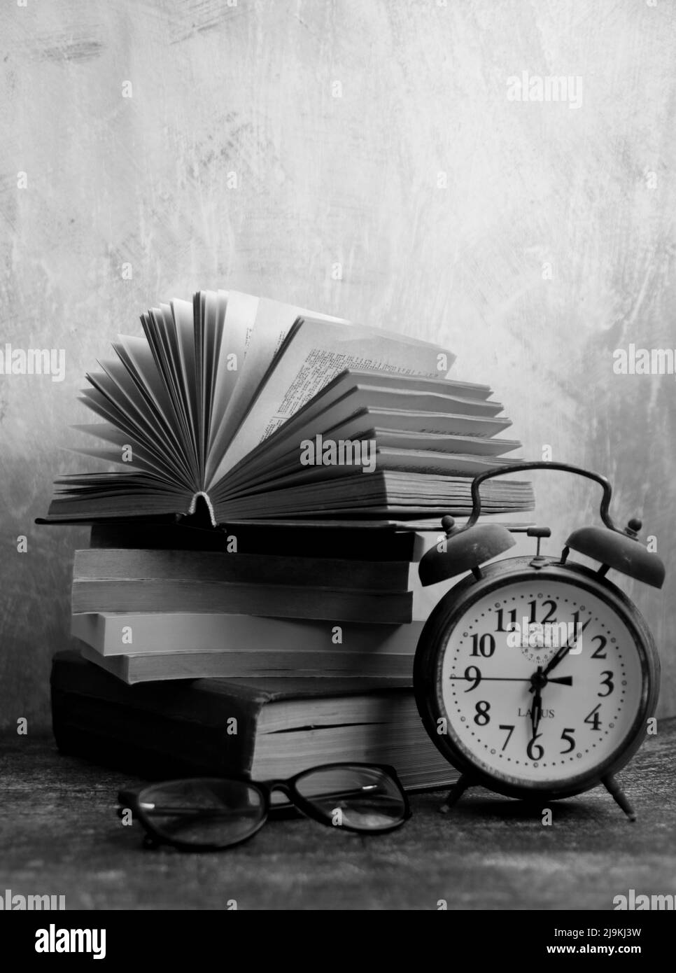 Still life with vintage mechanical alarm clock. Retro objects on grey background with copy space. Stack of old books close up photo. Stock Photo