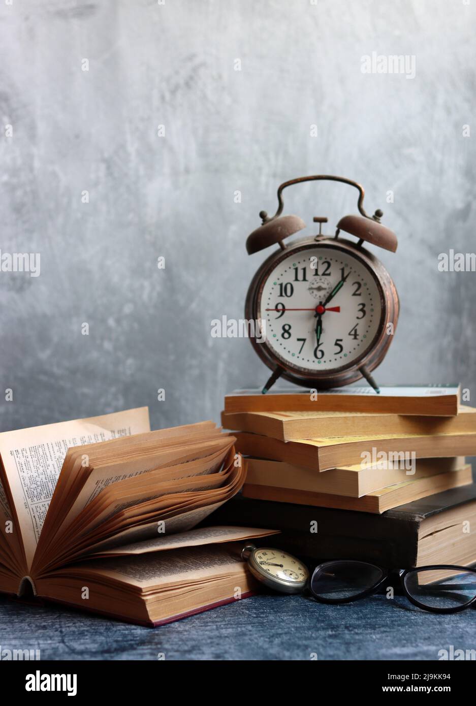 Stack of old books, vintage watch on a desk. Light grey textured background with copy space. Education concept. Stock Photo