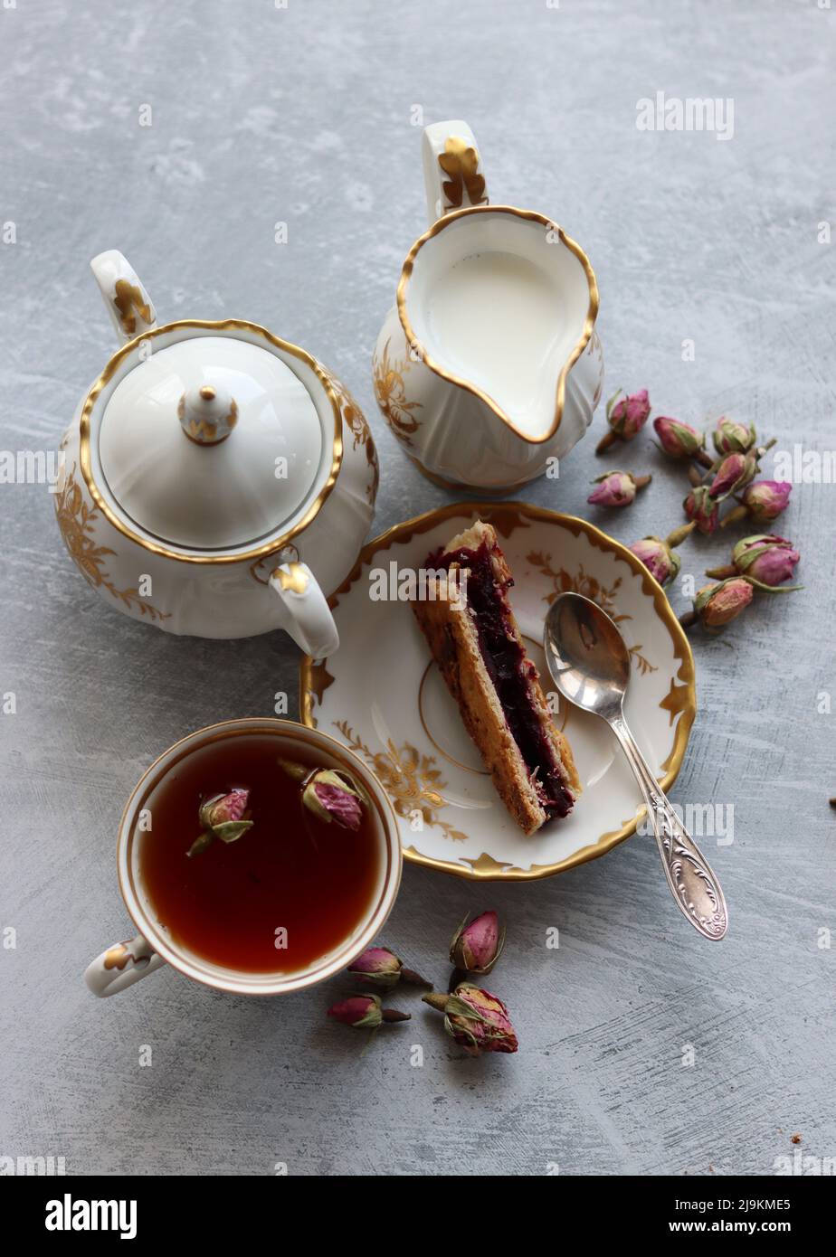 Still life with cup of tea,  jug of milk, cherry pie, small rose flowers. White vintage tableware on a table.  Sweet breakfast close up photo. Stock Photo