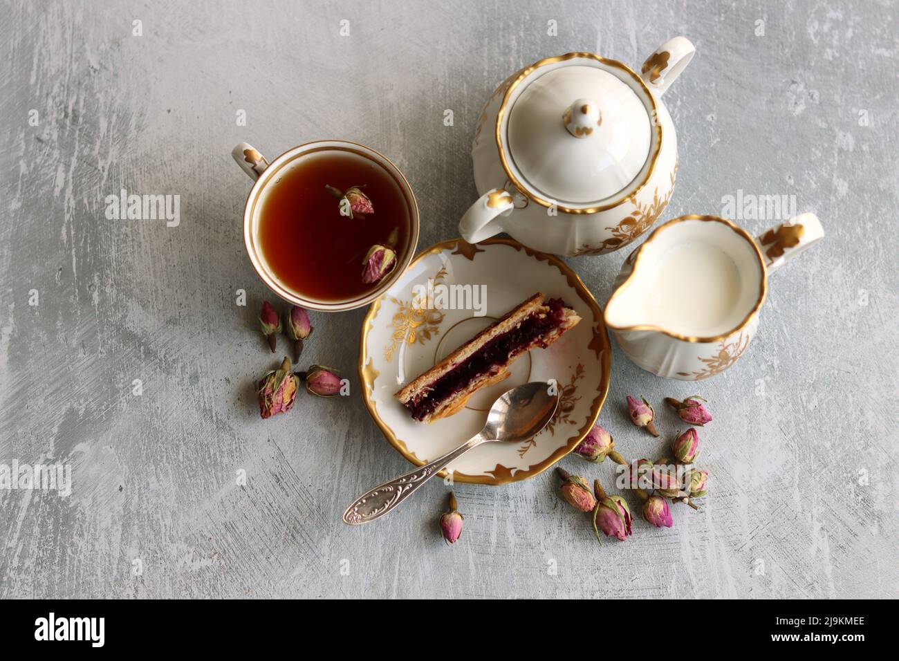 Still life with cup of tea,  jug of milk, cherry pie, small rose flowers. White vintage tableware on a table.  Sweet breakfast close up photo. Stock Photo