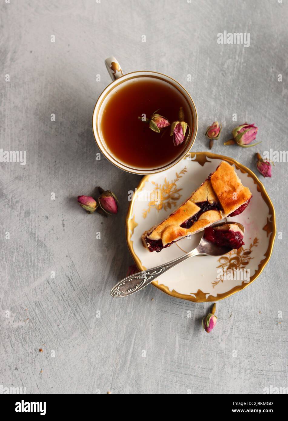 Still life with cup of tea,  jug of milk, cherry pie, small rose flowers. White vintage tableware on a table.  Sweet breakfast close up photo. Stock Photo