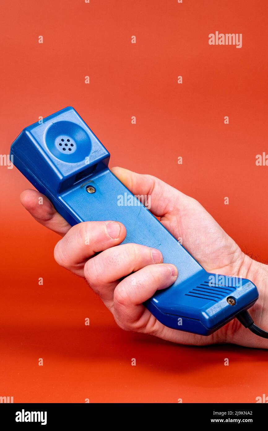 Vertical image of a hand with a landline phone, on an orange background. Stock Photo