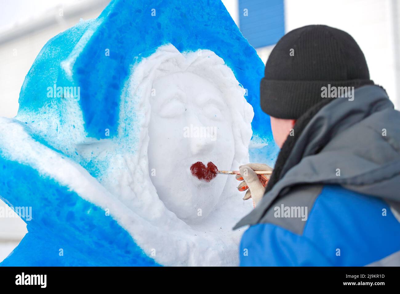 The master paints the figure of a snow woman on the street on a winter day. Production of New Year and Christmas figures on the eve of the holiday. Traditional hero or character Russian snow maiden. Stock Photo