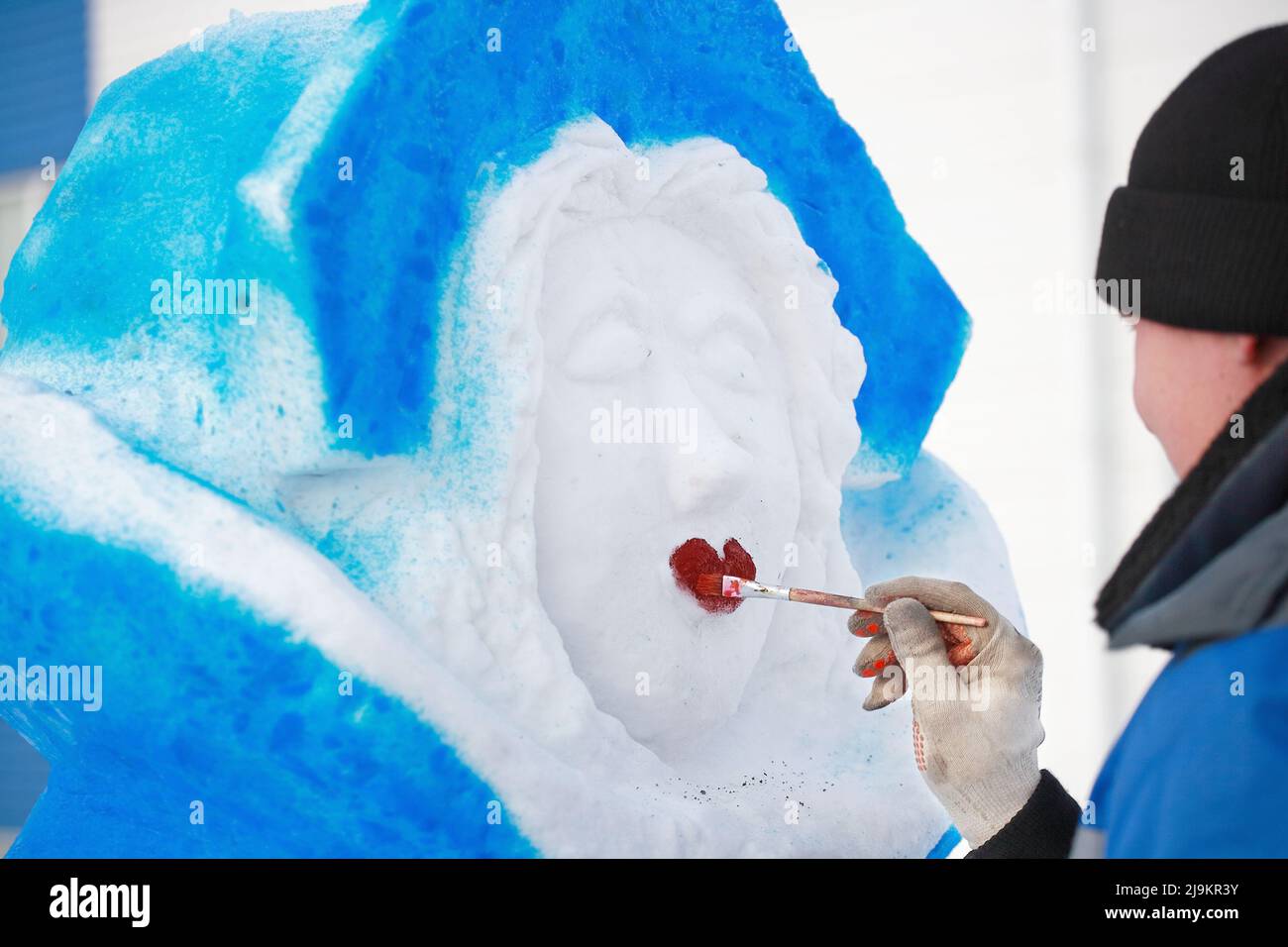 The master paints the figure of a snow woman on the street on a winter day. Production of New Year and Christmas figures on the eve of the holiday. Traditional hero or character Russian snow maiden. Stock Photo