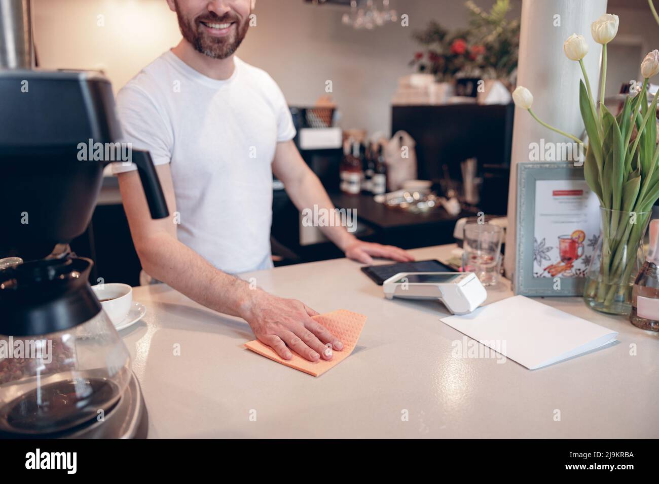 Cleaning counter at cafeteria concept. Male barista working at bar and keep it clean. Stock Photo