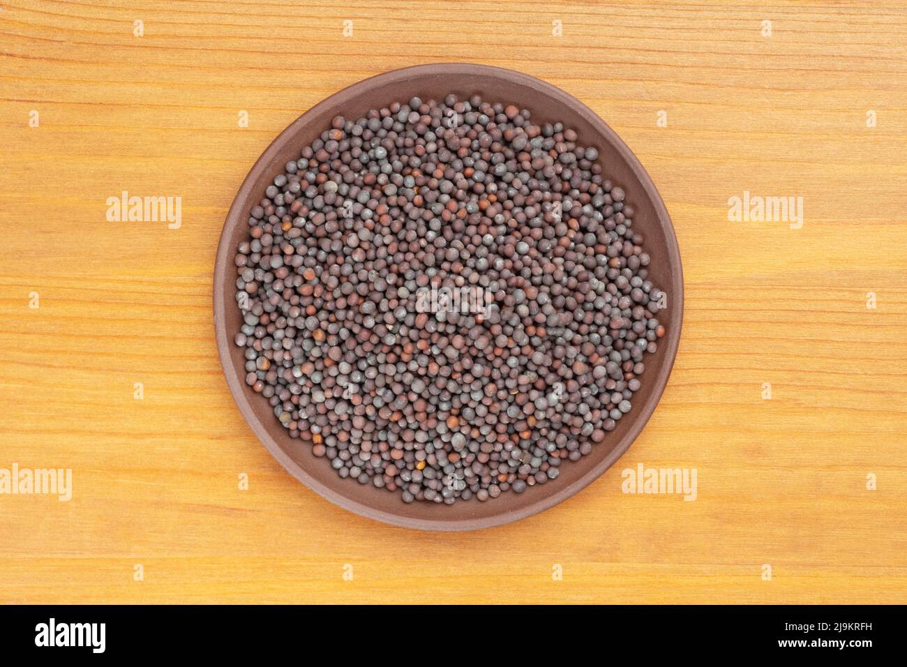 Spice Mustard seeds (Brassica juncea) in brown clay plate on yellow wooden background. Close up. Vegetarian food concept Stock Photo