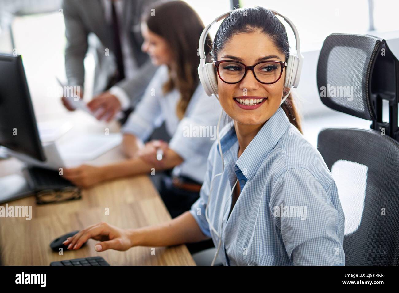 Smiling friendly female call-center agent with headset working on support hotline in the office Stock Photo