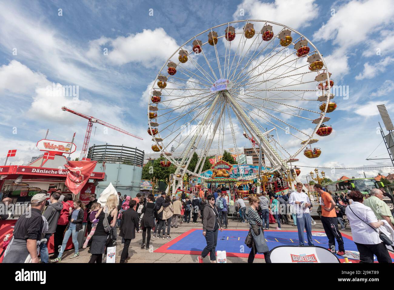 People enjoy fun fair and ferris wheel in Augustusplatz town square during the Wave-Gothic event, Leipzig. Stock Photo