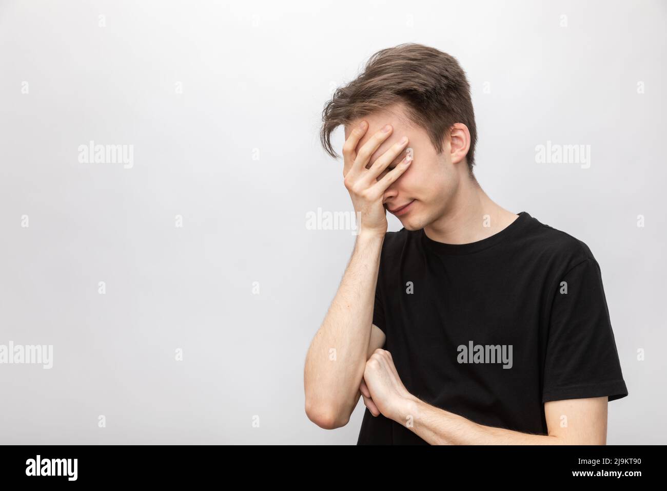 Portrait of young man wearing black tshirt covering his eyes and face with palm. Studio shot on gray background Stock Photo