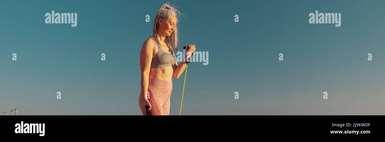 Woman in sportswear exercising on the sports site, using rubber bands Stock Photo
