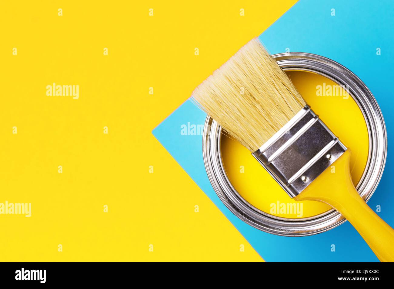 Can of yellow paint with brush on yellow and blue background. Top view, redecorating concept. Stock Photo