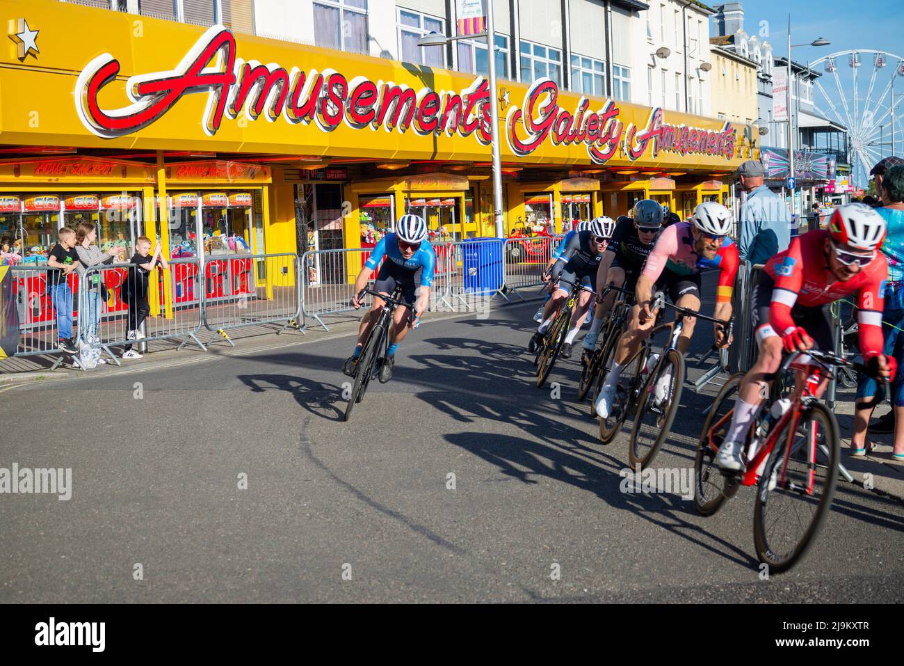 Cyclists racing in the Sportsbreaks Tour Series Men's cycle race round five in Clacton on Sea, Essex, UK. Criterium street race passing amusements Stock Photo