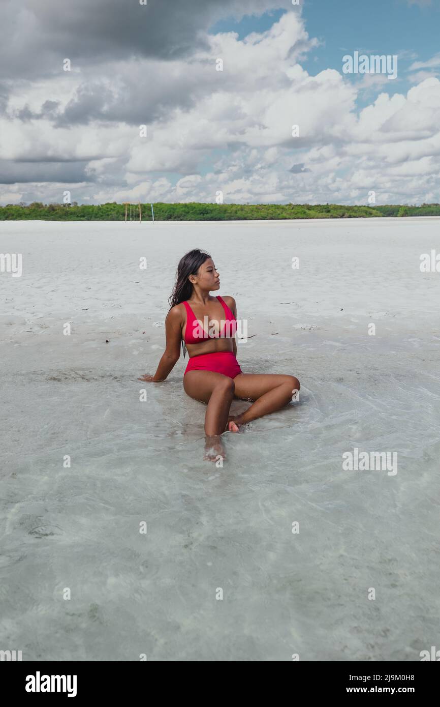 young tan asian model with a red bikini swimsuit laying on Leebong private island with a pristine white sand beach and green mangrove on a sunny day Stock Photo