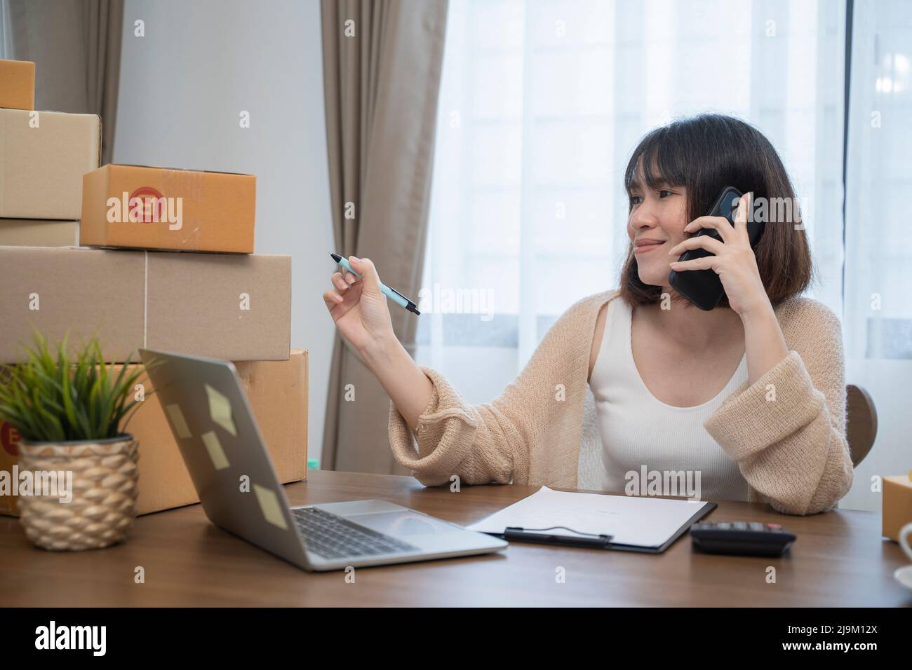 Young Asian female using her laptop and working at home, Small business female owner or Start up small business entrepreneur working online marketing Stock Photo
