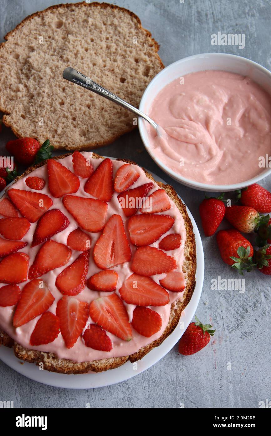 Strawberry cake in process. Close up photo of strawberry tart ingredients on a table. Fresh berries, dairy cream, cake layers top view. Stock Photo