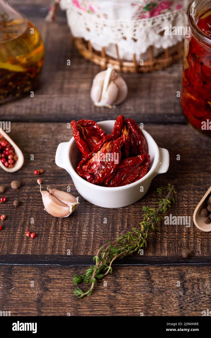 Sun-dried tomatoes in olive oil in a white bowl with pepper, garlic and thyme in a rustic style. Selective focus, close-up. Stock Photo
