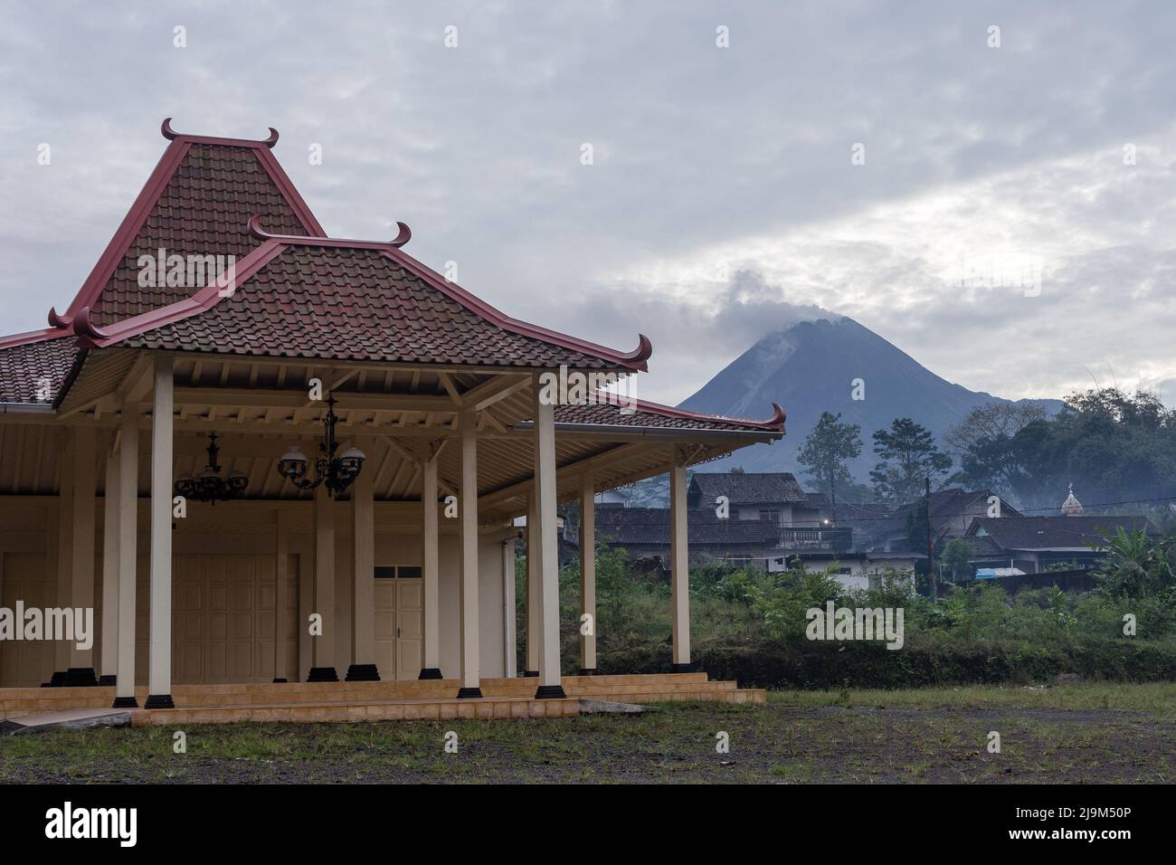 Mount Merapi spews volcanic ashes and materials as seen from Girikerto village in Sleman, Yogyakarta, Indonesia with Joglo Pendopo building. Stock Photo