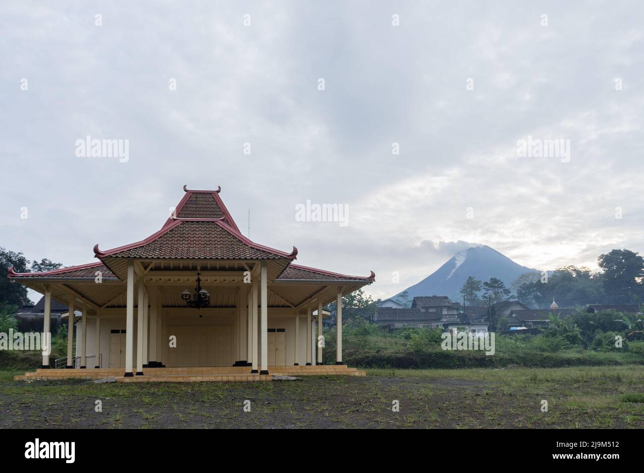 Mount Merapi spews volcanic ashes and materials as seen from Girikerto village in Sleman, Yogyakarta, Indonesia with Joglo Pendopo building. Stock Photo