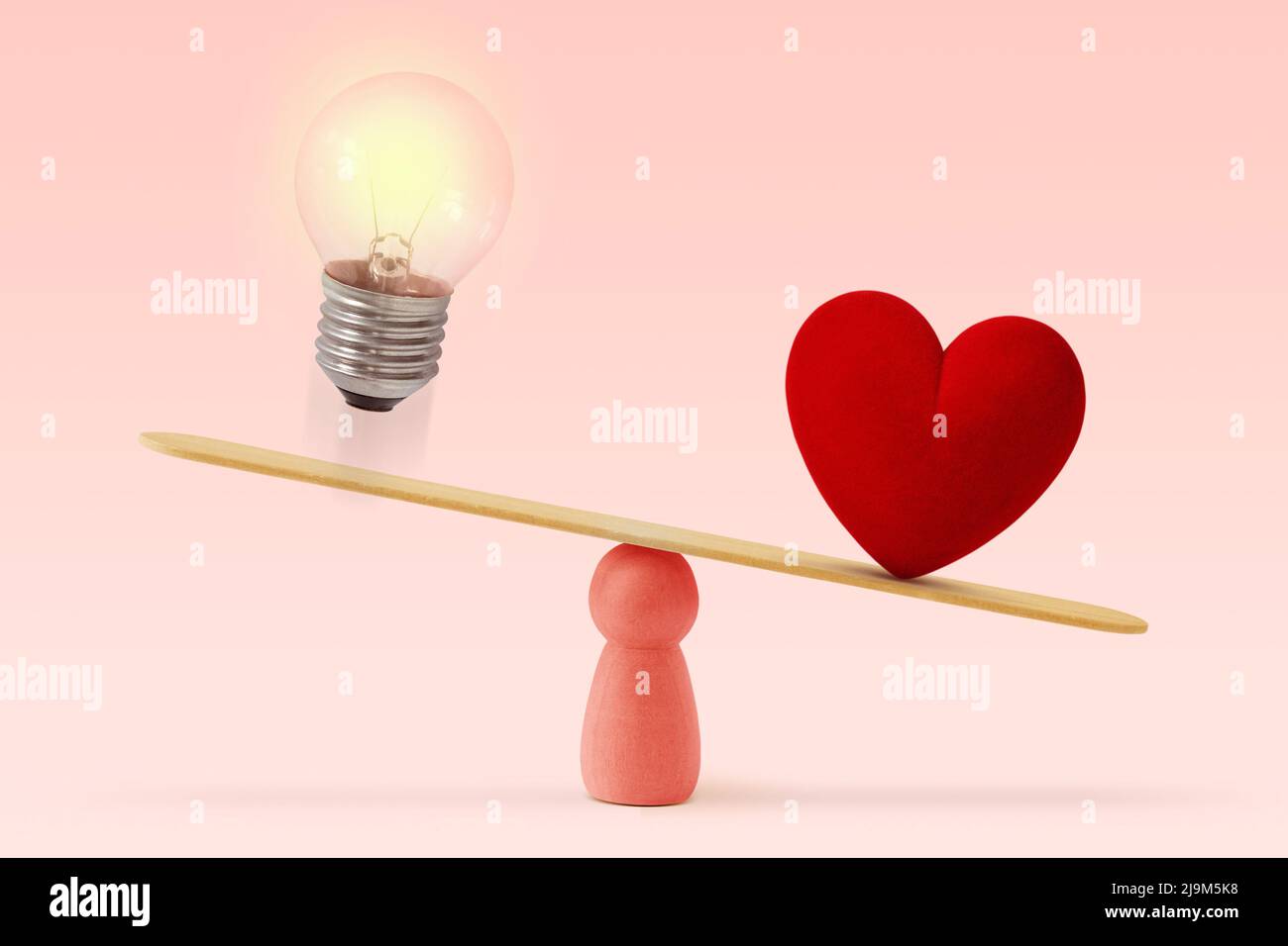 Light bulb and heart on scale on pink background - Concept of woman and love priority over brain in life Stock Photo