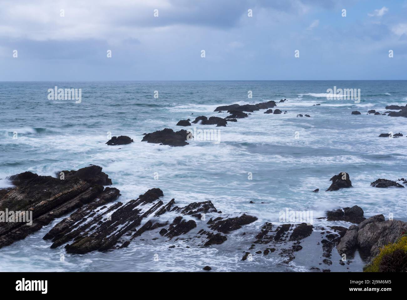 Long exposure of the ocean near the Point Arena Lighthouse on a partly cloudy sky day with featuring a row of rocks going into the horizon Stock Photo