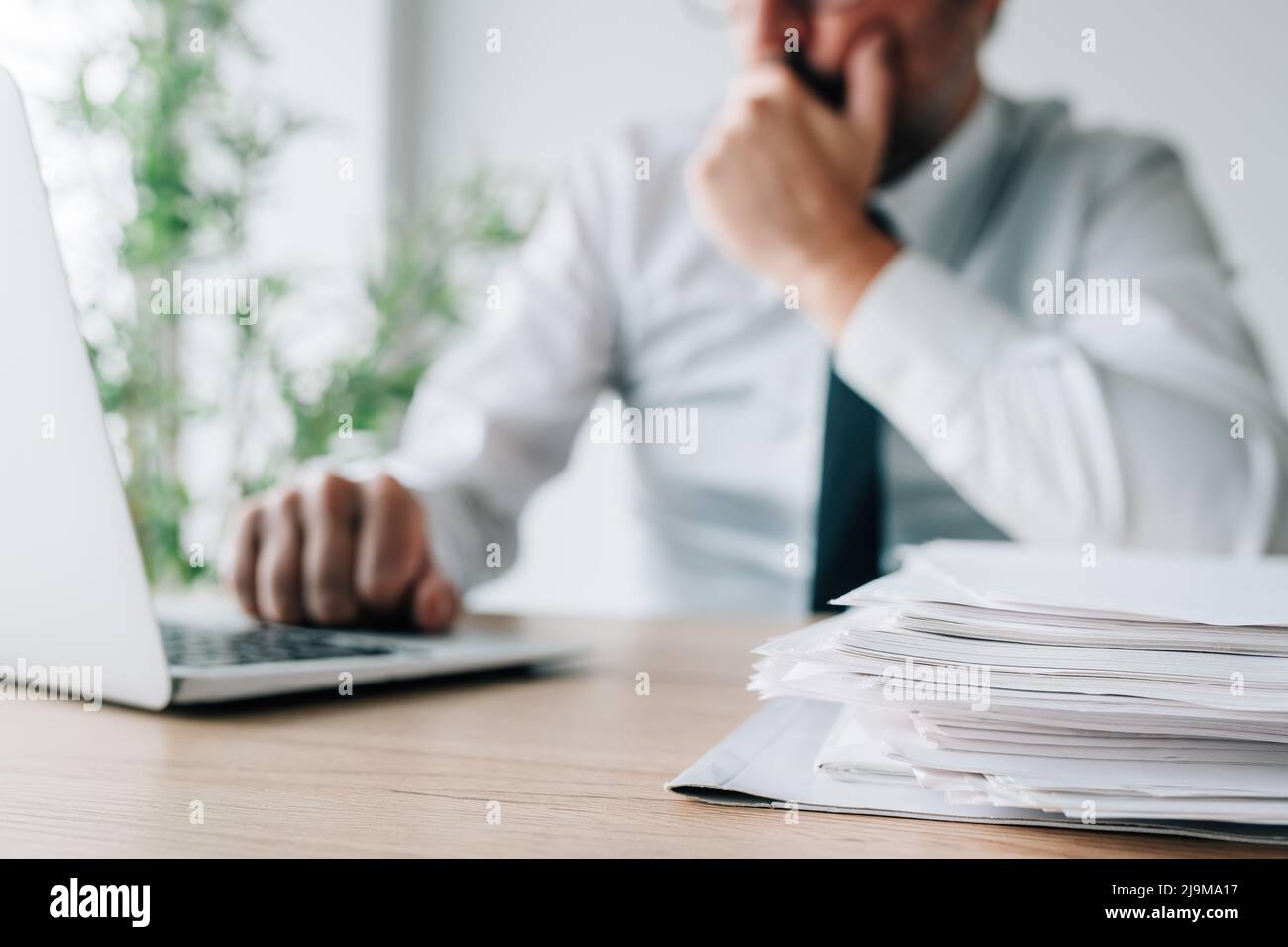 Choosing the best candidate, employer with job applications and cv papers piled on office desk looking at laptop screen, selective focus Stock Photo