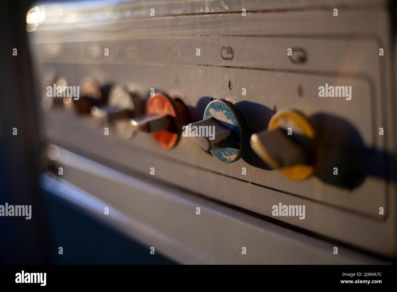 Old gas stove in the kitchen. Knobs for adjusting the gas supply. Morning light falls on a vintage fire plate. Stock Photo