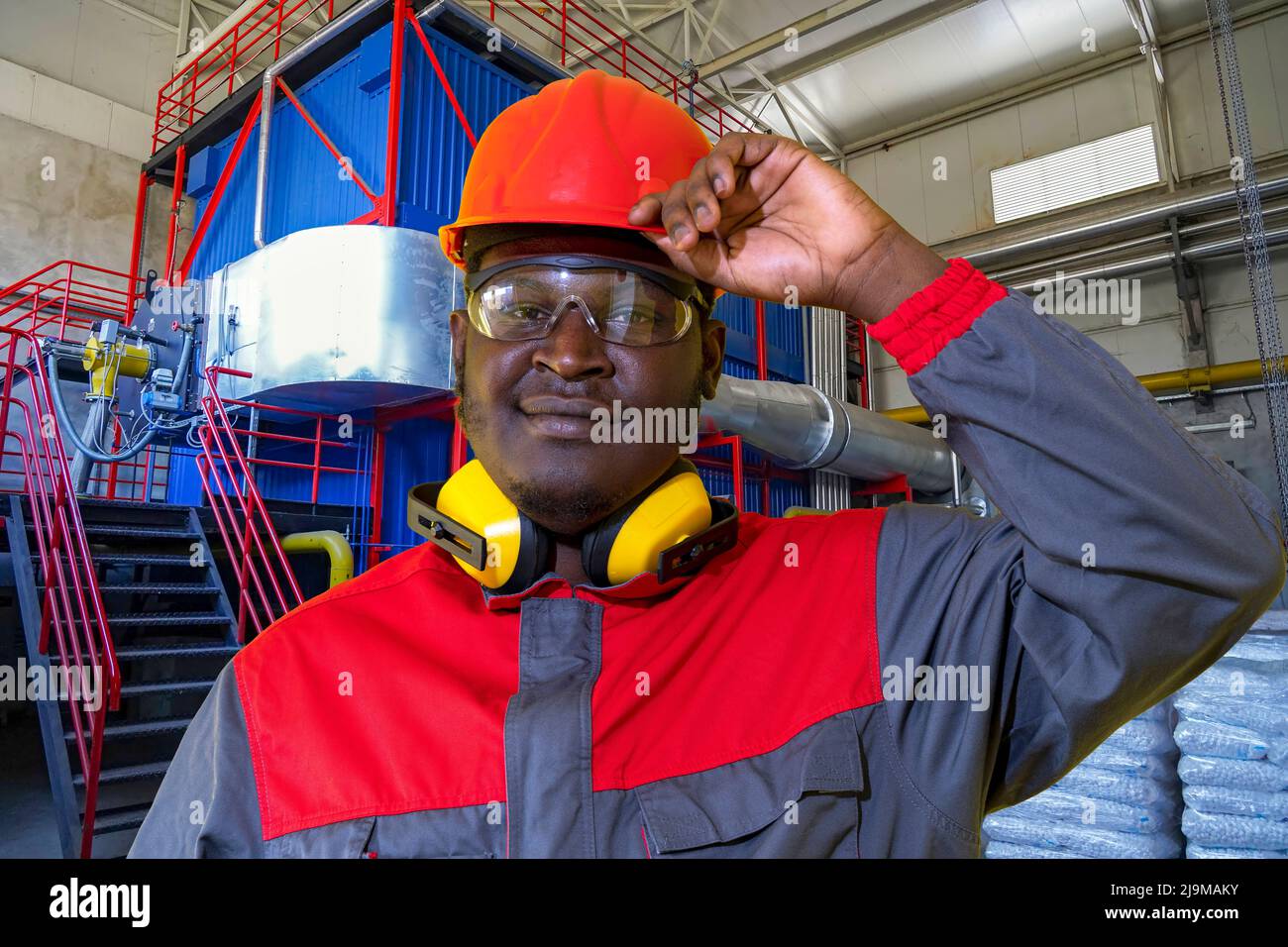 Black Industrial Worker In Red Helmet, Protective Eyewear, Hearing  Protection Equpiment And Work Uniform Looking At Camera Stock Photo - Alamy