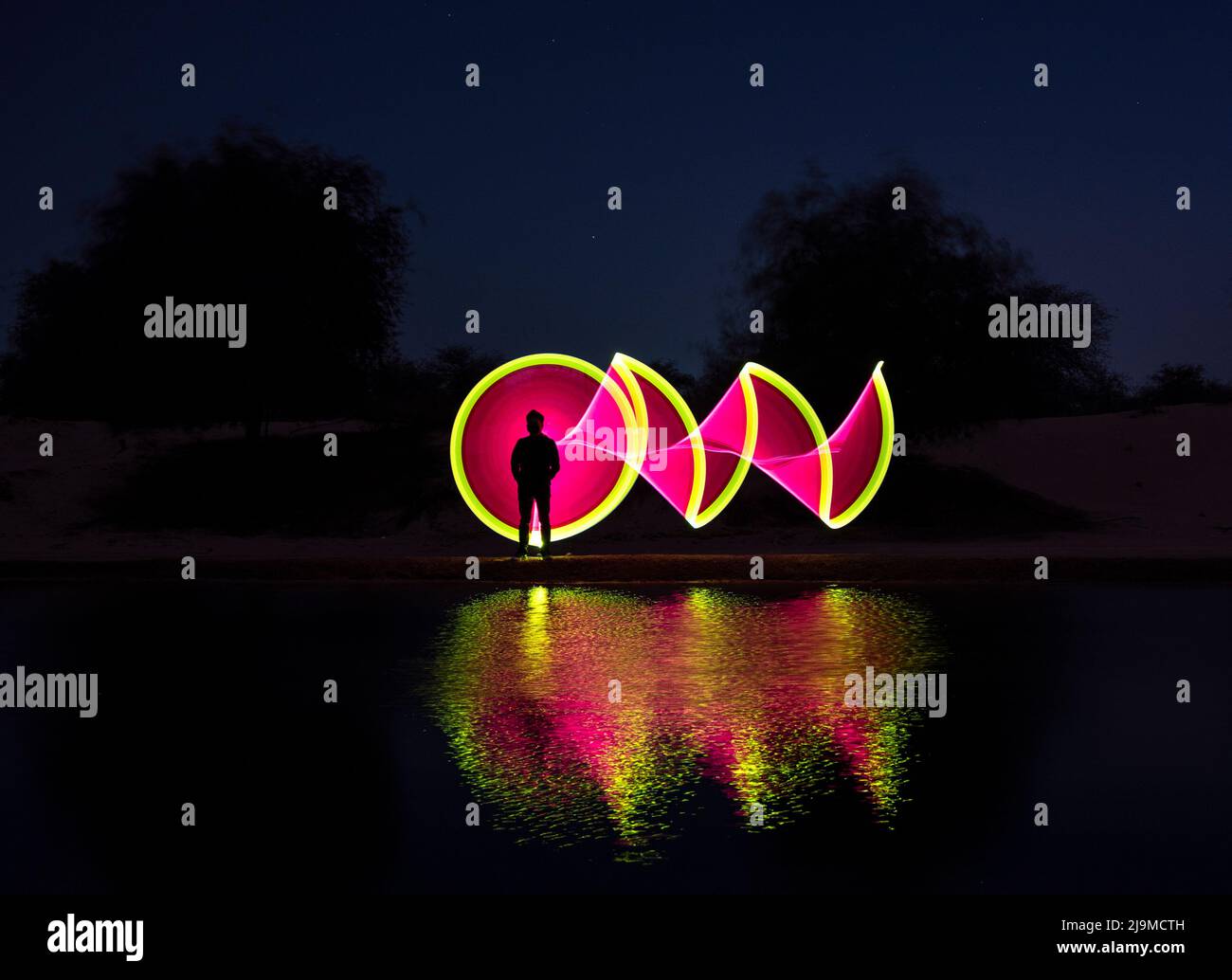 A colorful light painting in dark with multicoloured led lights throwing beautiful reflections in the water captured at the Al qudra lake , Dubai ,UAE Stock Photo