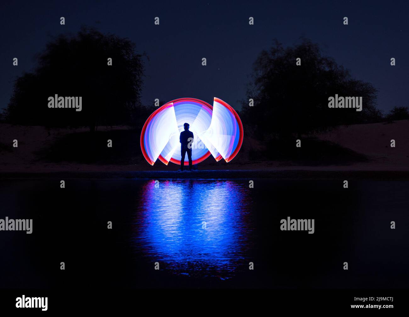 A colorful light painting of a man dressed up like an astronaut  with multicoloured led lights throwing beautiful reflections in the water Stock Photo