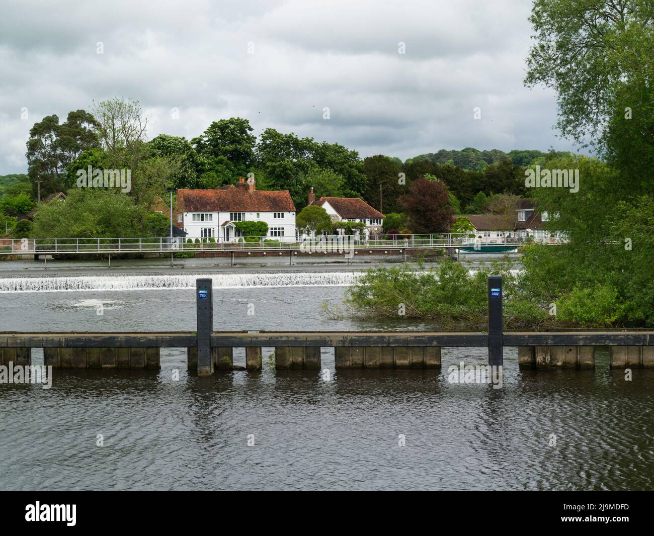 View across a weir at Mill End village on River Thames to riverside whitewashed cottages with red roofs next to Hambledon Mill Buckinghamshire England Stock Photo