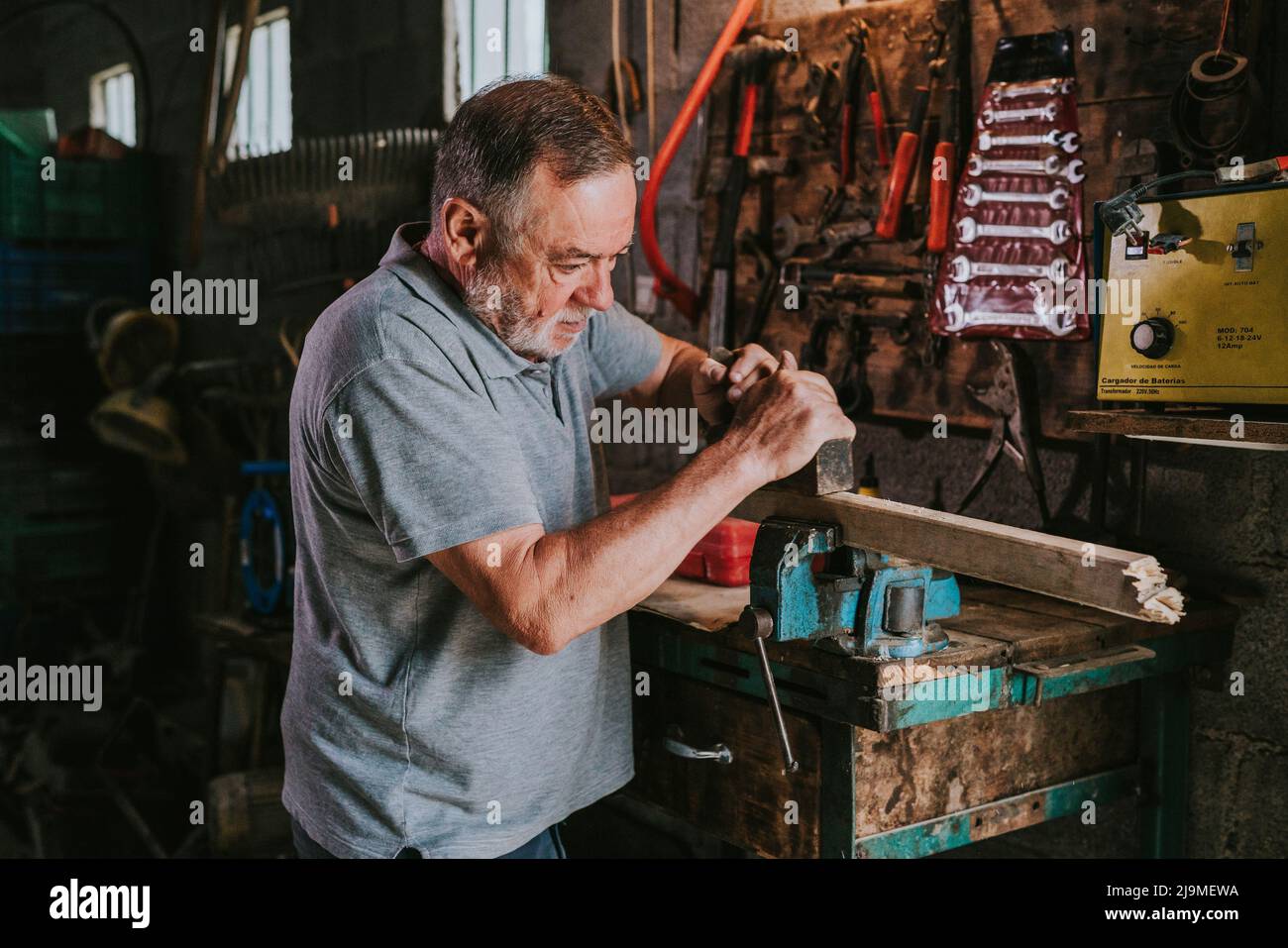 Focused mature male woodworker using jointer for planning wooden plank