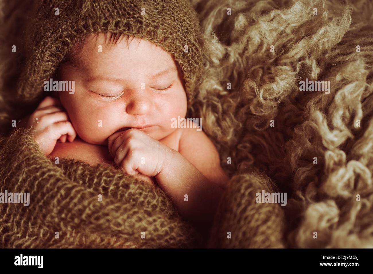 From above of adorable newborn baby with dark hair wrapped in blanket lying on soft fur plaid in light studio Stock Photo